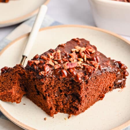 A slice of coca cola cake on a plate with a bite on a fork next to it.