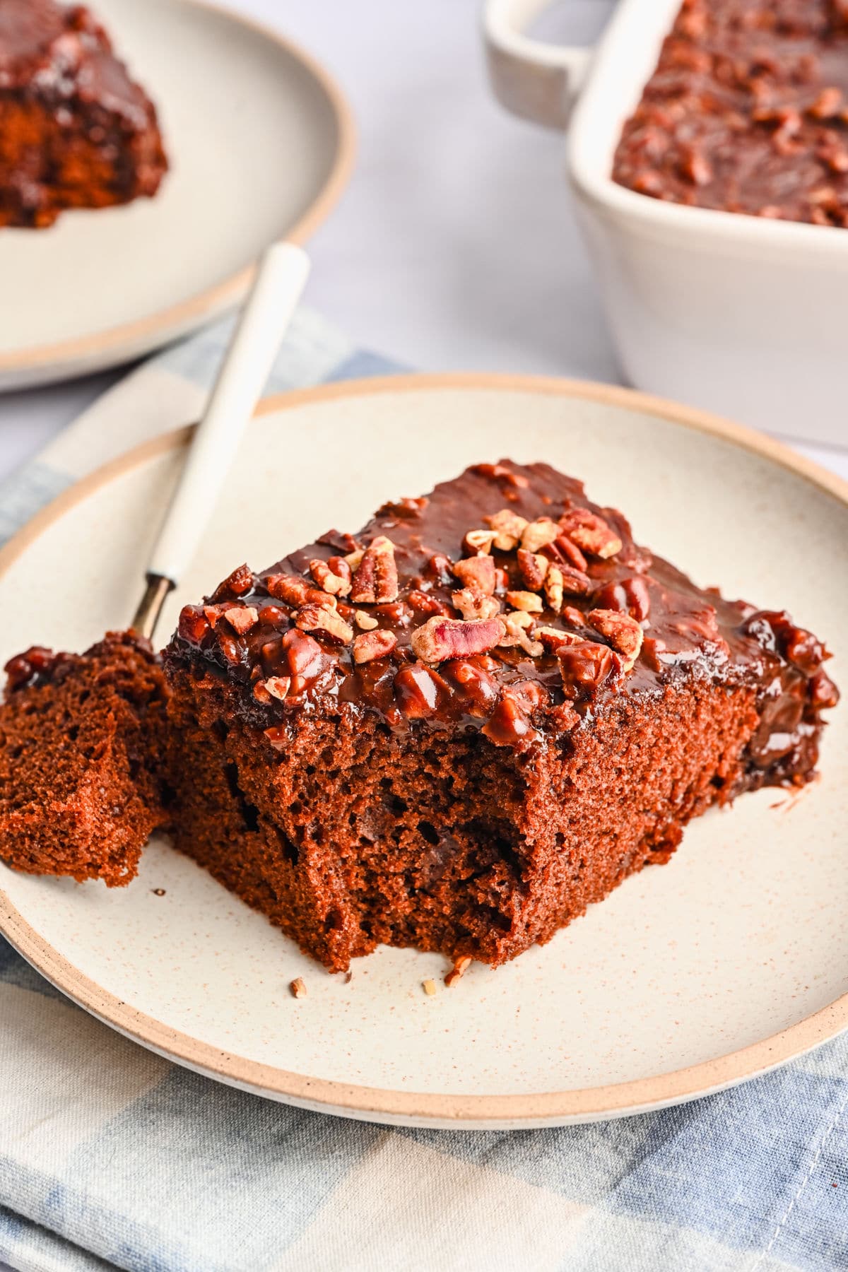 A slice of coca cola cake on a plate with a bite on a fork next to it.