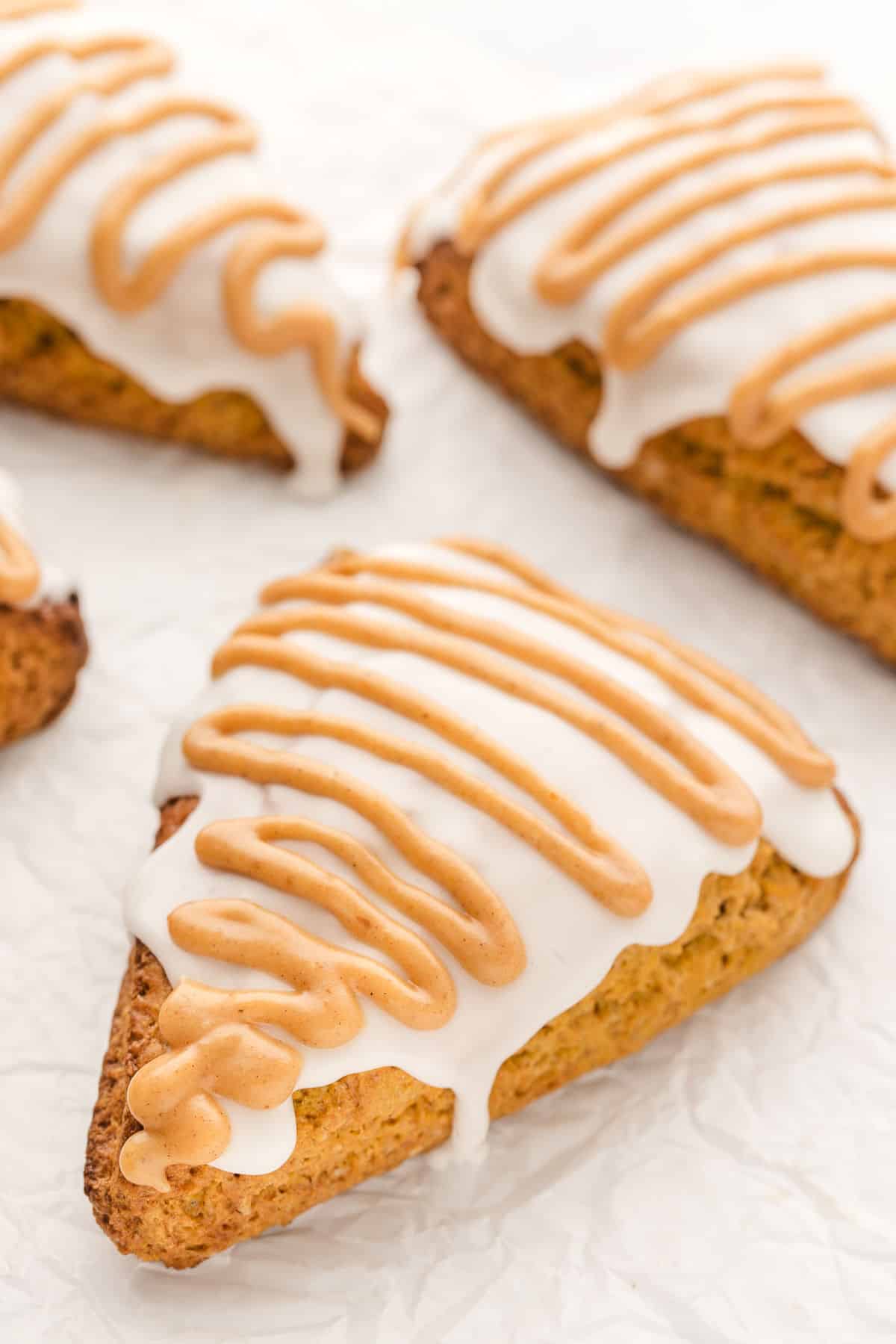 Three pumpkin scones on a piece of white parchment paper.