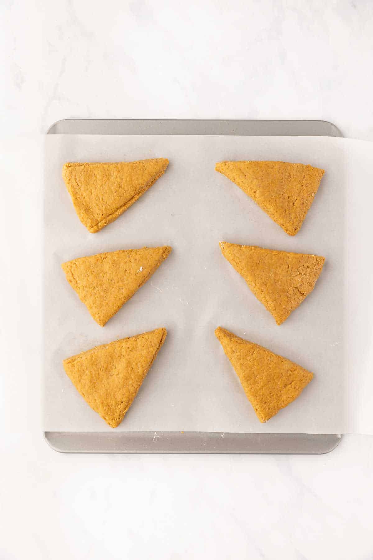 Six unbaked pumpkin scones on a parchment lined baking sheet. 