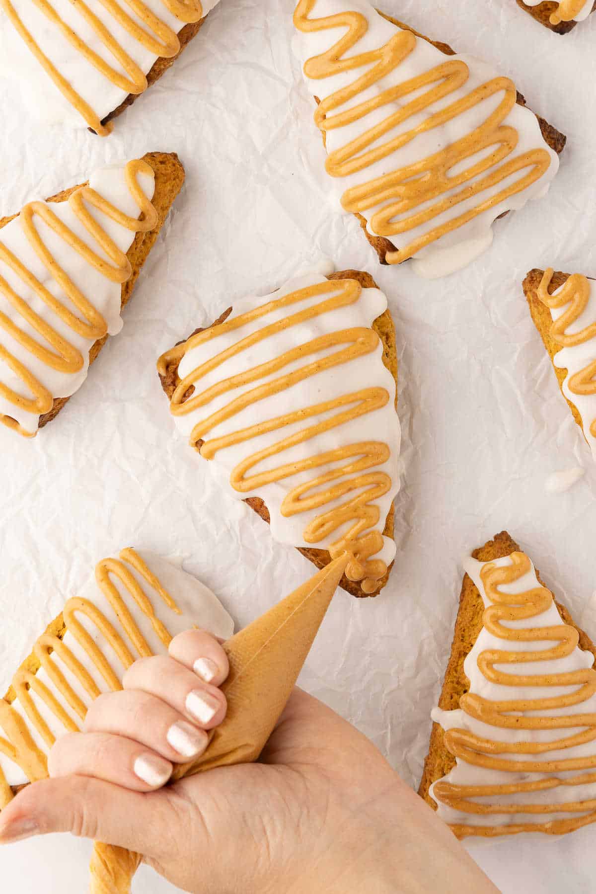 A piping bag piping pumpkin glaze onto the top of a pumpkin scone.