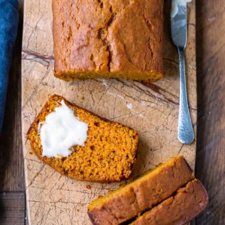 Partially buttered slice of pumpkin bread on a marble butting board.