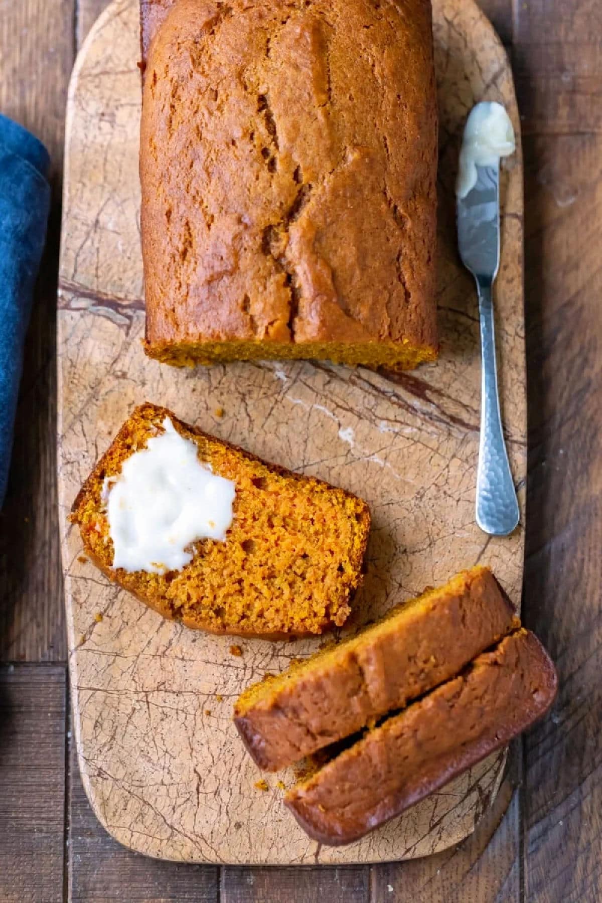 Partially buttered slice of pumpkin bread on a marble butting board.