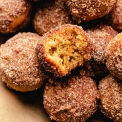 A wooden tray of baked apple cider donut holes with one with a bite out of it.