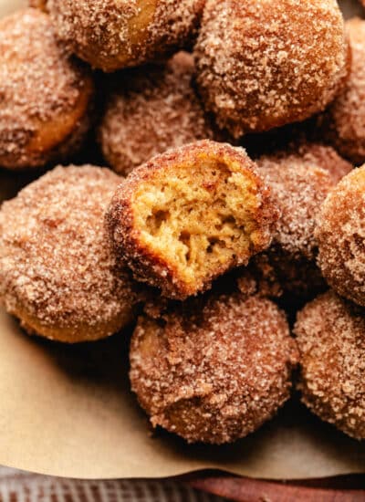 A wooden tray of baked apple cider donut holes with one with a bite out of it.