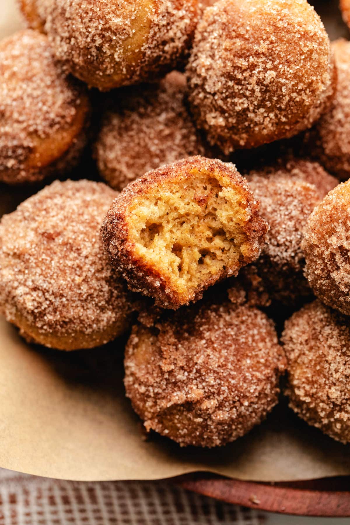 A wooden tray of baked apple cider donut holes with one with a bite out of it.