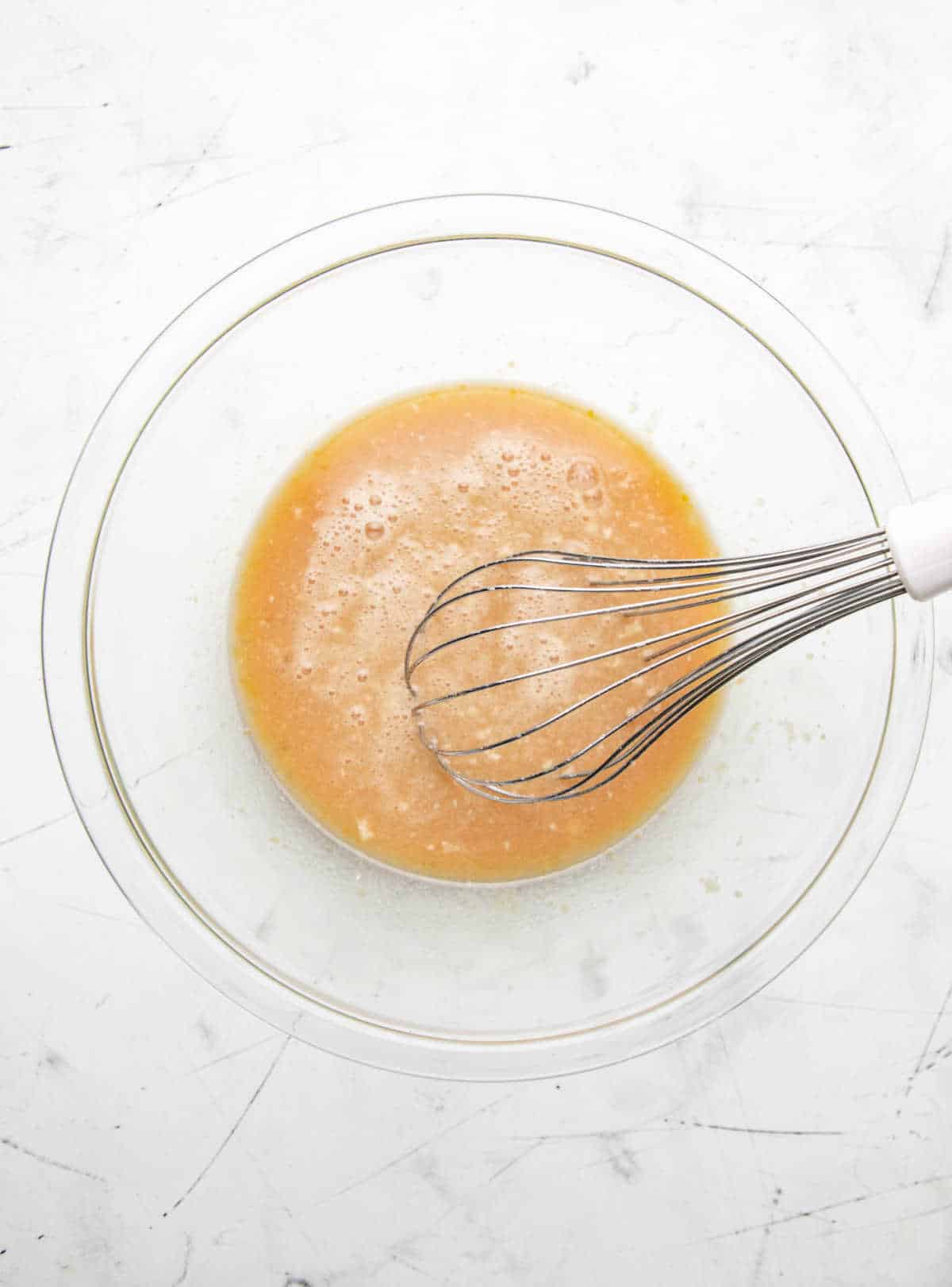 Melted butter whisked into apple cider mixture in a glass mixing bowl.