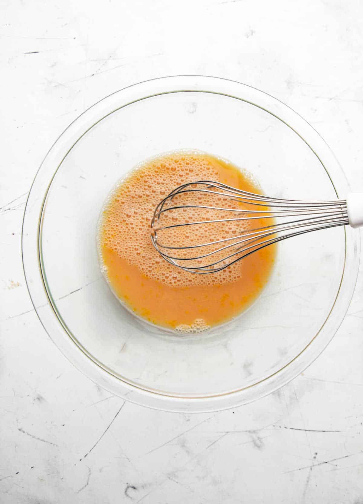 Apple cider mixture in a glass mixing bowl with a whisk in it.