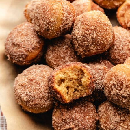 A wooden cake stand lined with brown parchment paper with a stack of baked apple cider donut holes on top.