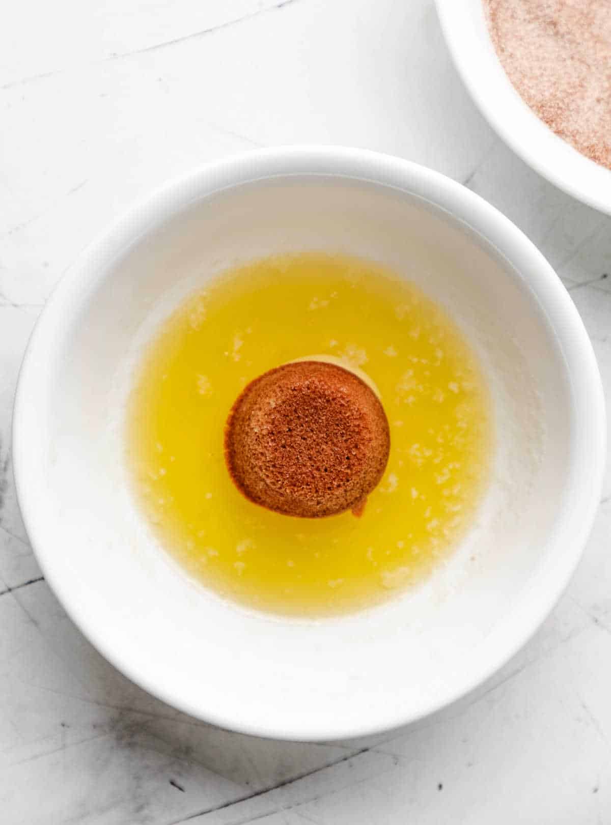 A baked apple cider donut hole in a dish of melted butter. 