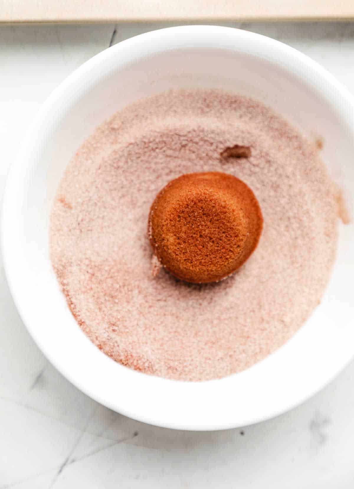 A baked apple cider donut hole in a dish of cinnamon sugar.
