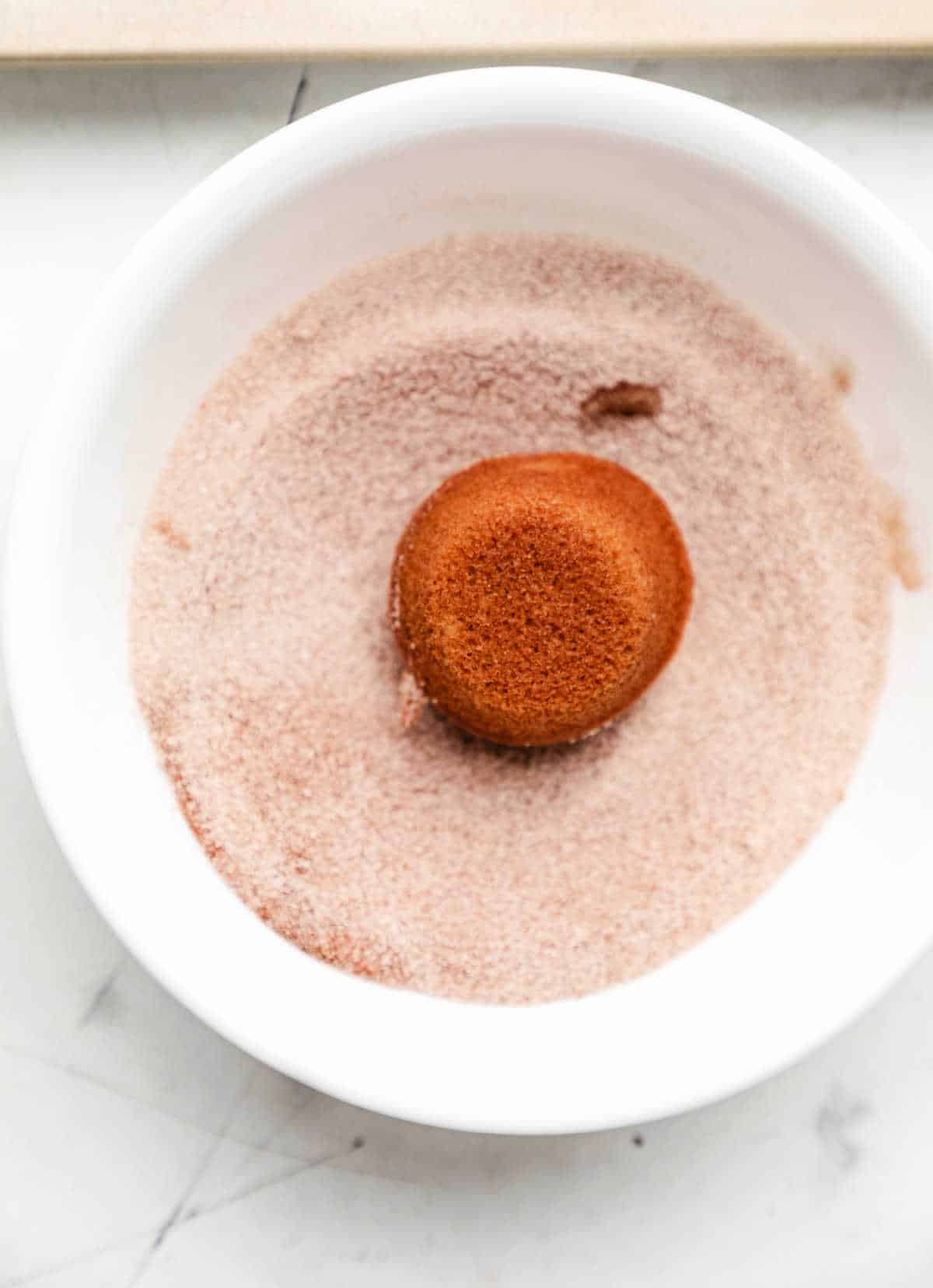 A baked apple cider donut hole in a dish of cinnamon sugar. 