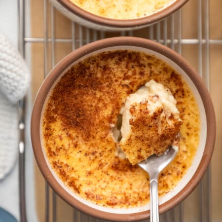 A silver spoon holding a scoop of baked custard in the custard cup.
