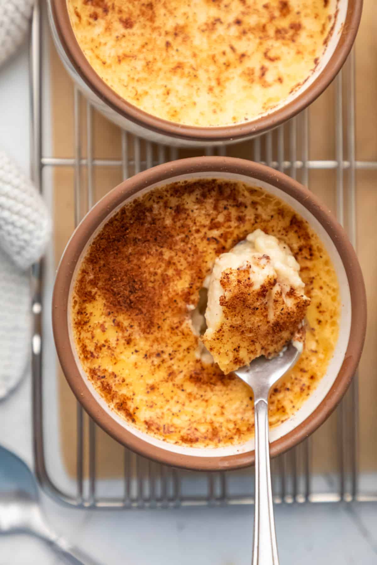 A silver spoon holding a scoop of baked custard in the custard cup.