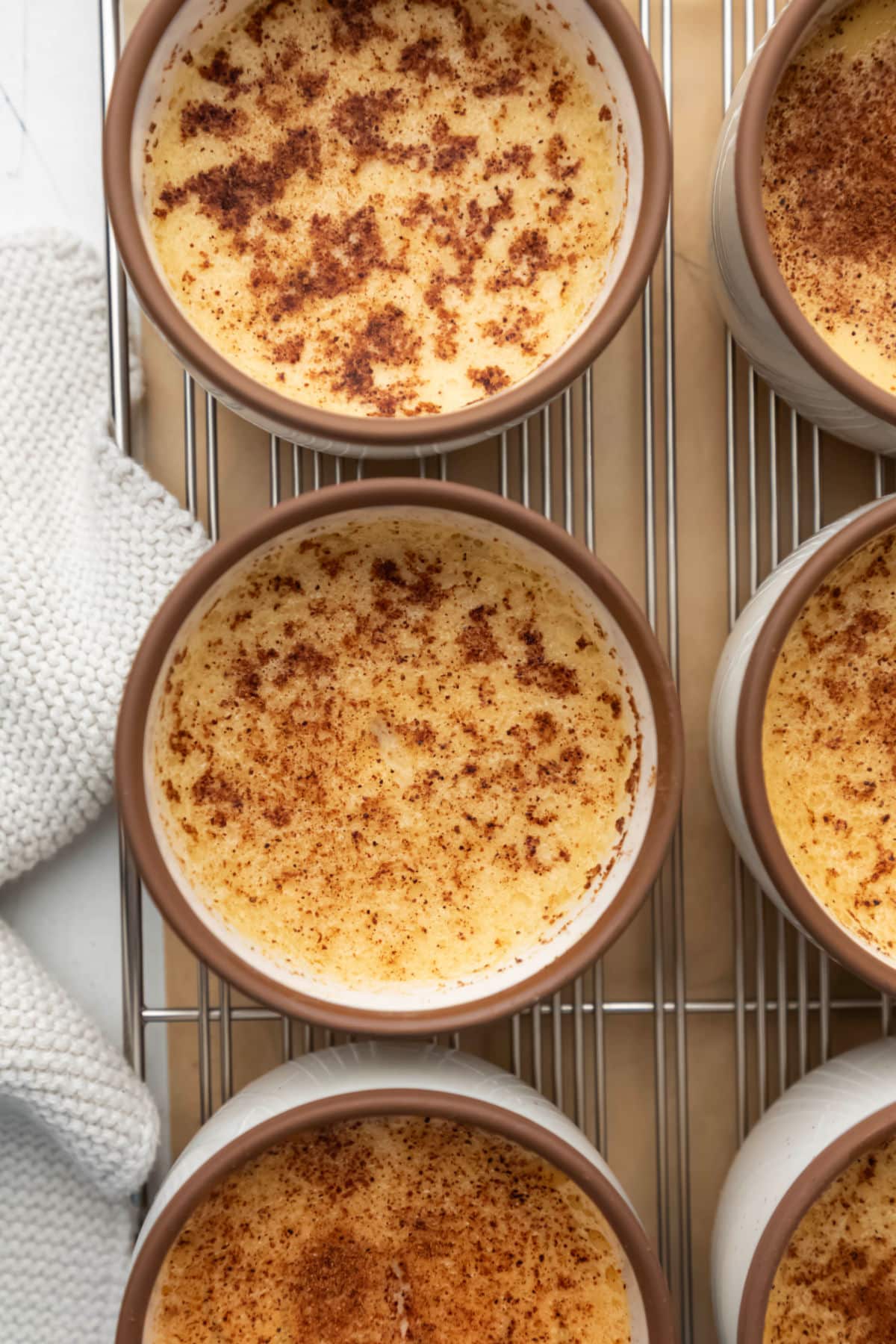 Rows of baked custard in custard cups on a wire cooling rack.
