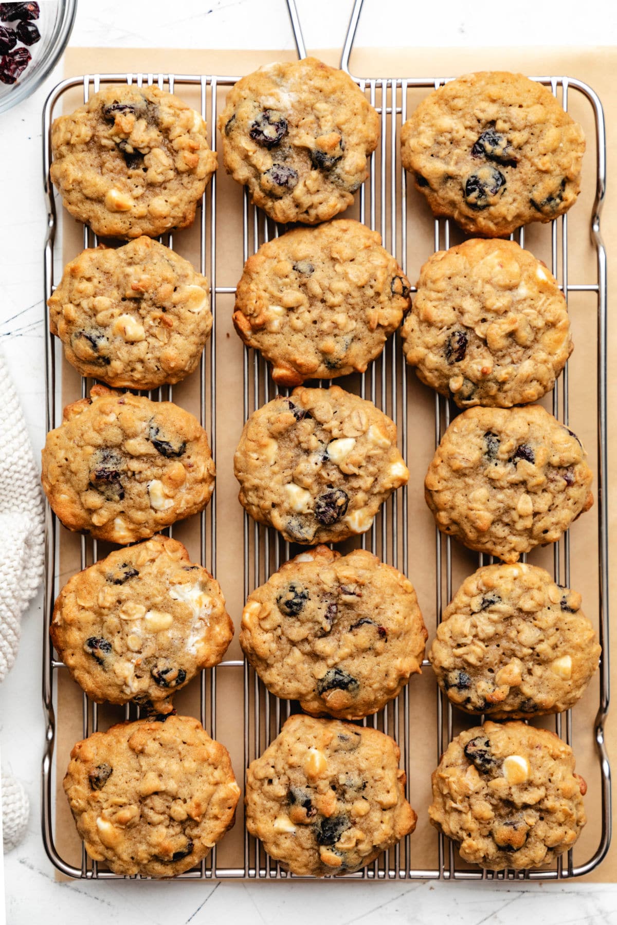 Fifteen cranberry oatmeal cookies on a wire cooling rack next to a dish of cranberries.