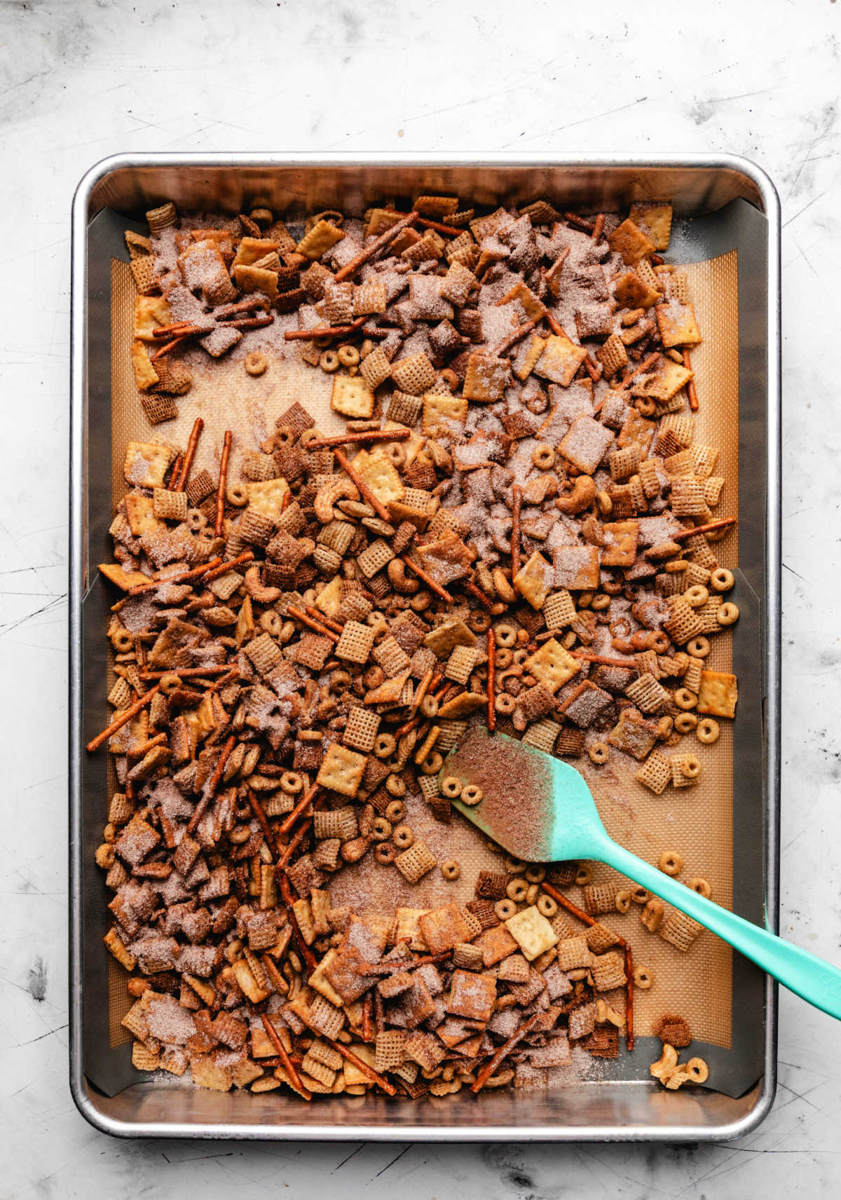 A rubber spatula stirring cinnamon sugar mixture into Chex mix.