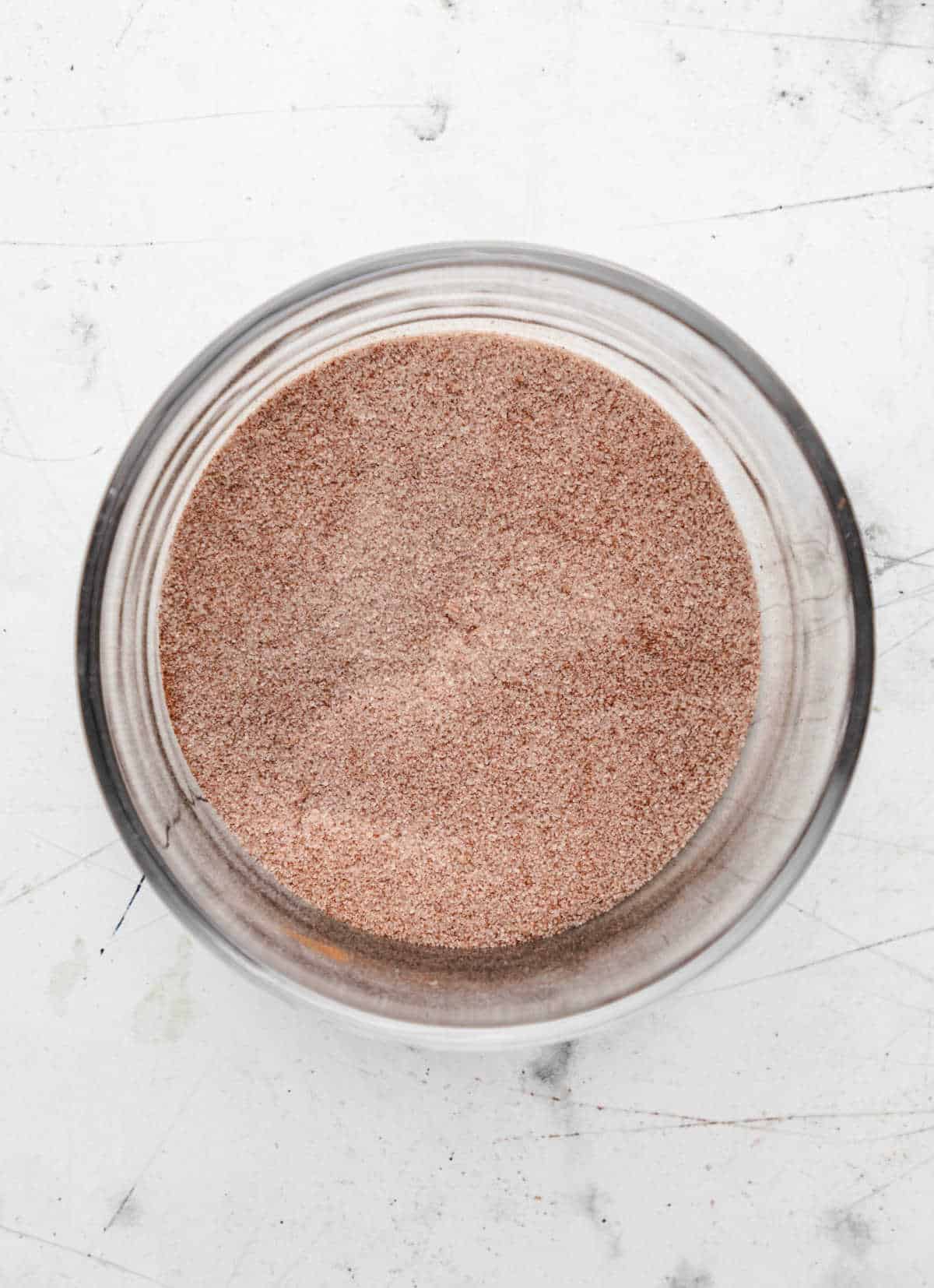 A glass dish of cinnamon sugar on a marble background.