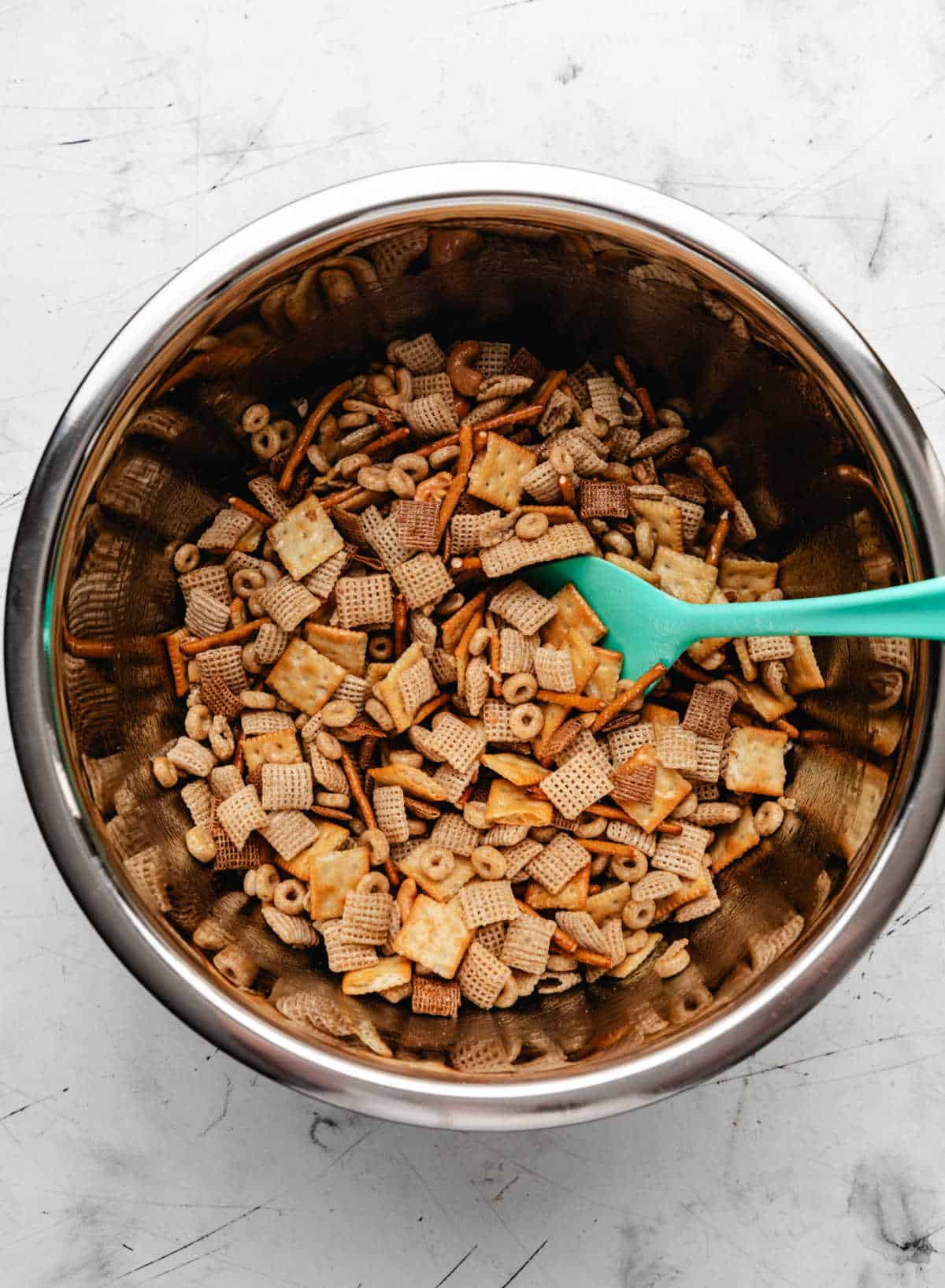 Honey butter mixture poured over cereal mixture in a steel mixing bowl. 