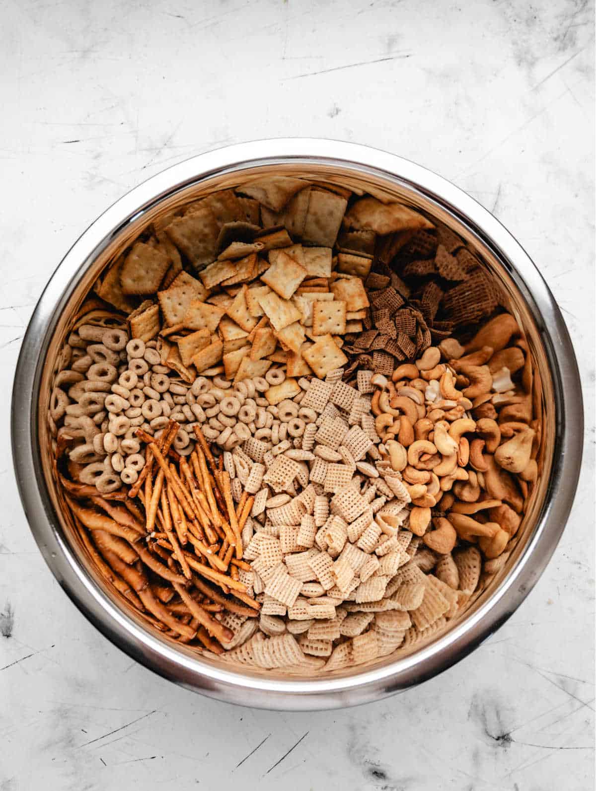 Cereal nuts pretzels and crackers in a stainless steel mixing bowl. 