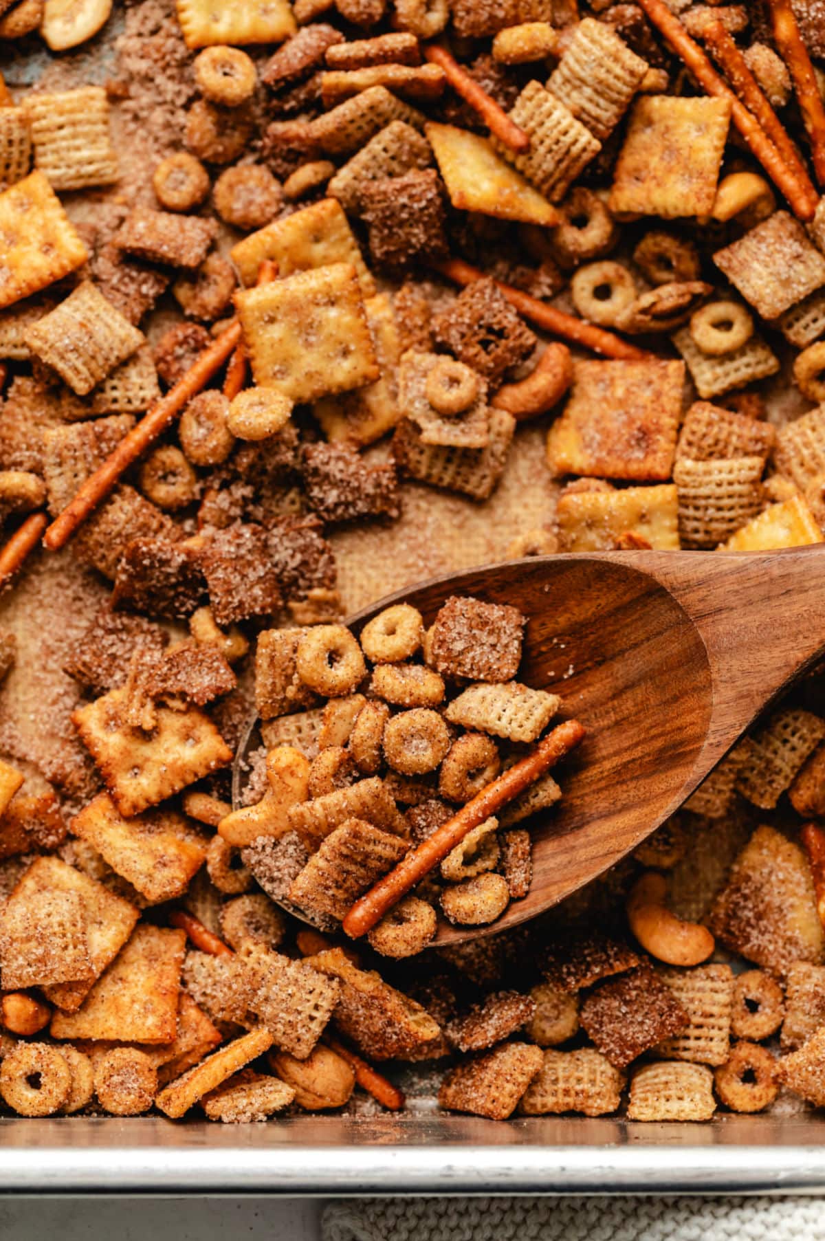 A wooden spoon in a tray of Sweet and Salty Chex mix.