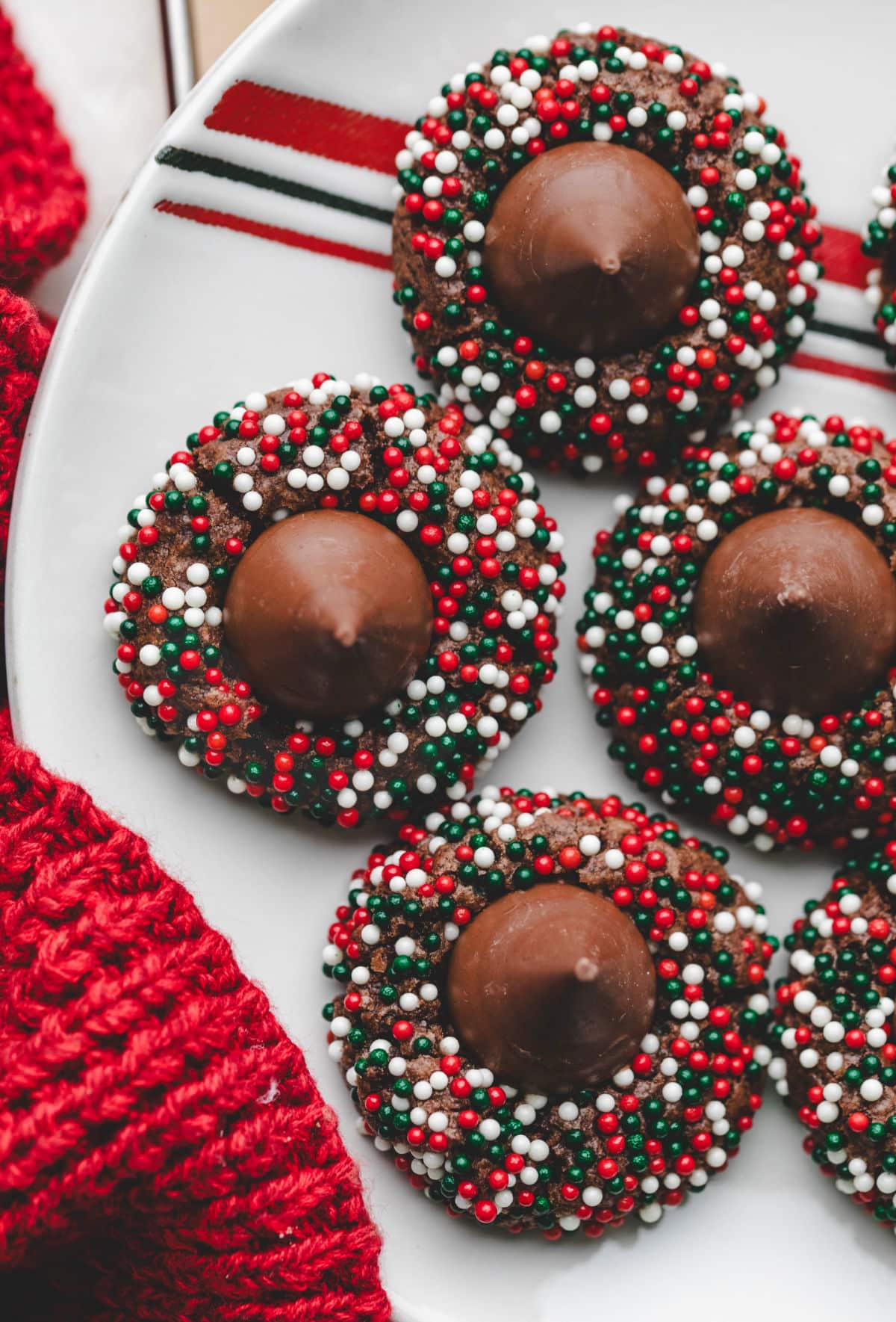 A white plate with red and green stripes holding Christmas kiss cookies. 