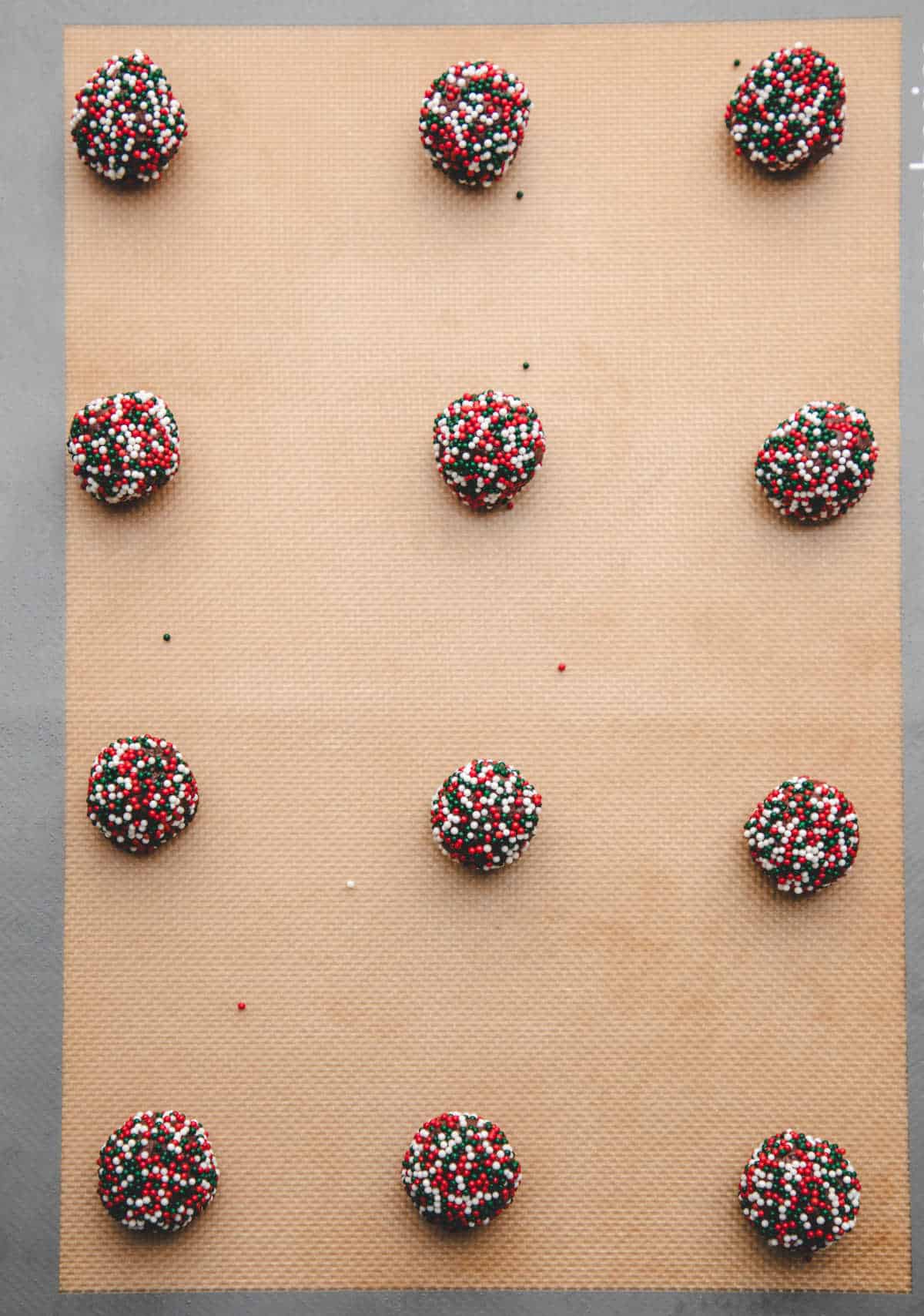 Balls of chocolate cookie dough rolled in sprinkles on a baking sheet. 