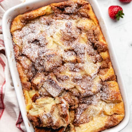 A wooden spoon holding a scoop of French toast casserole in a white baking pan.