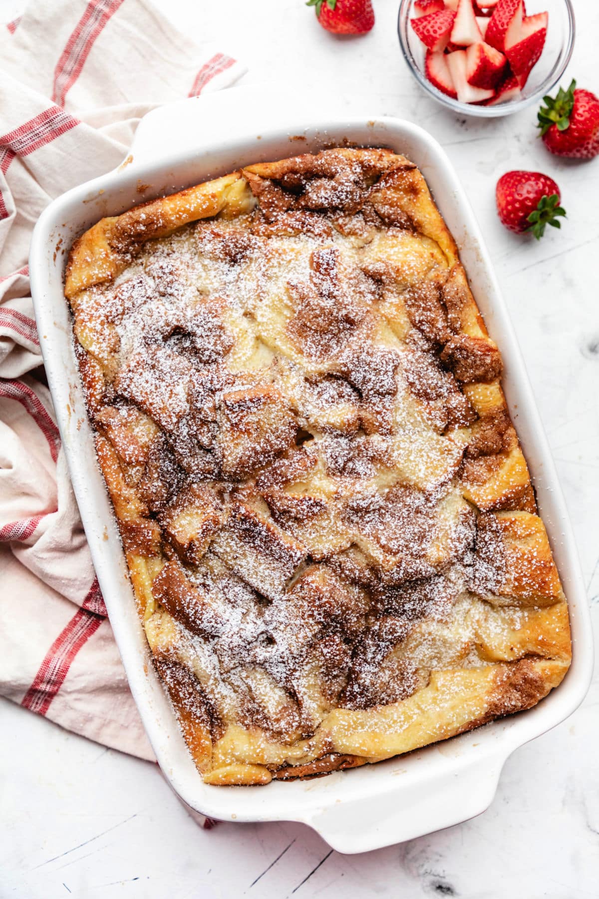 A baked French toast casserole next to fresh strawberries.