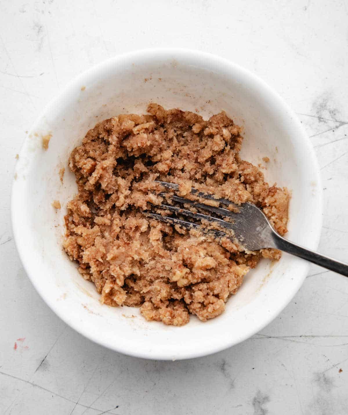 Butter and brown sugar mixed together with a fork in a white bowl. 