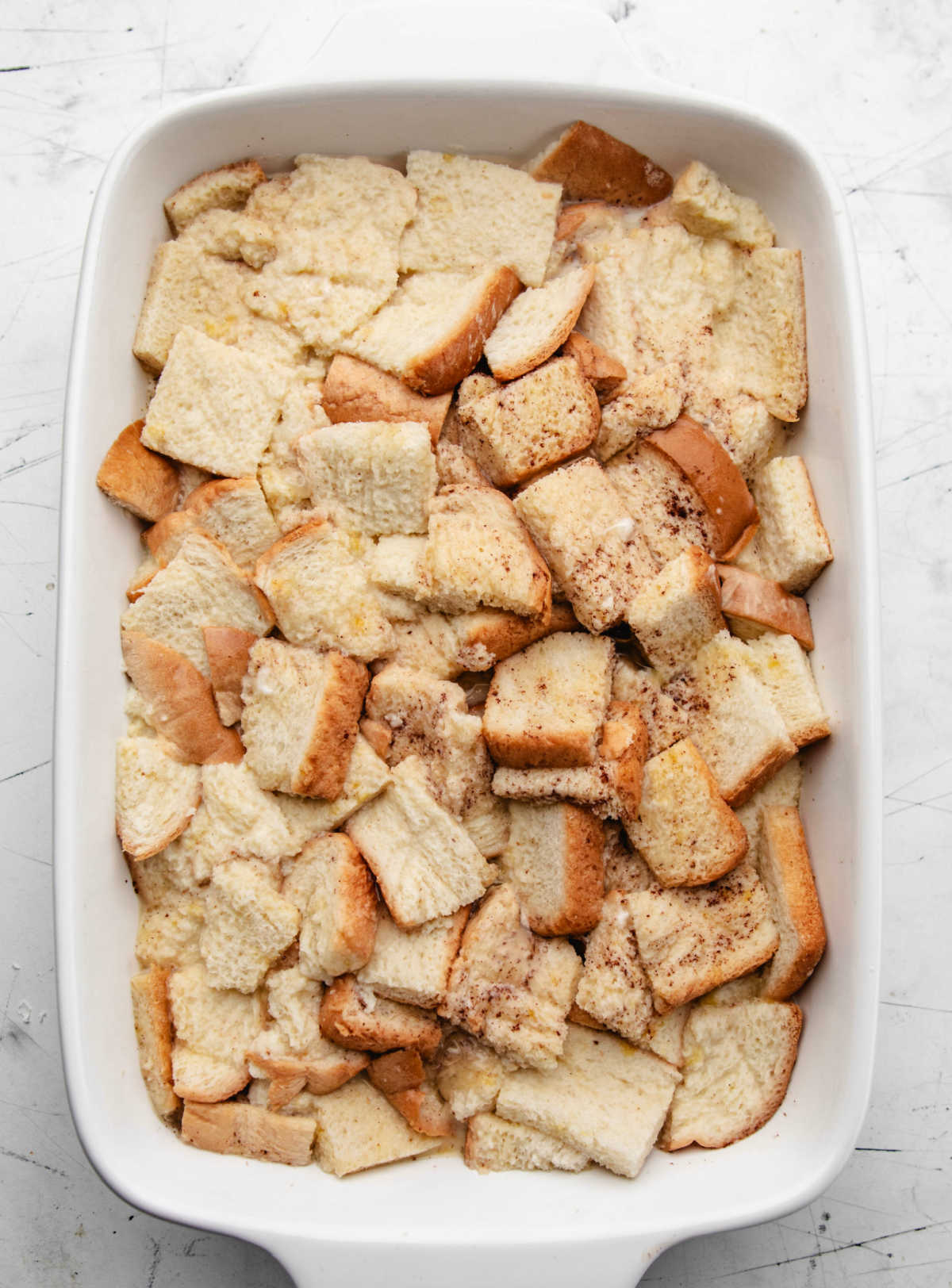 Egg mixture poured over cubed white bread in a white baking dish.