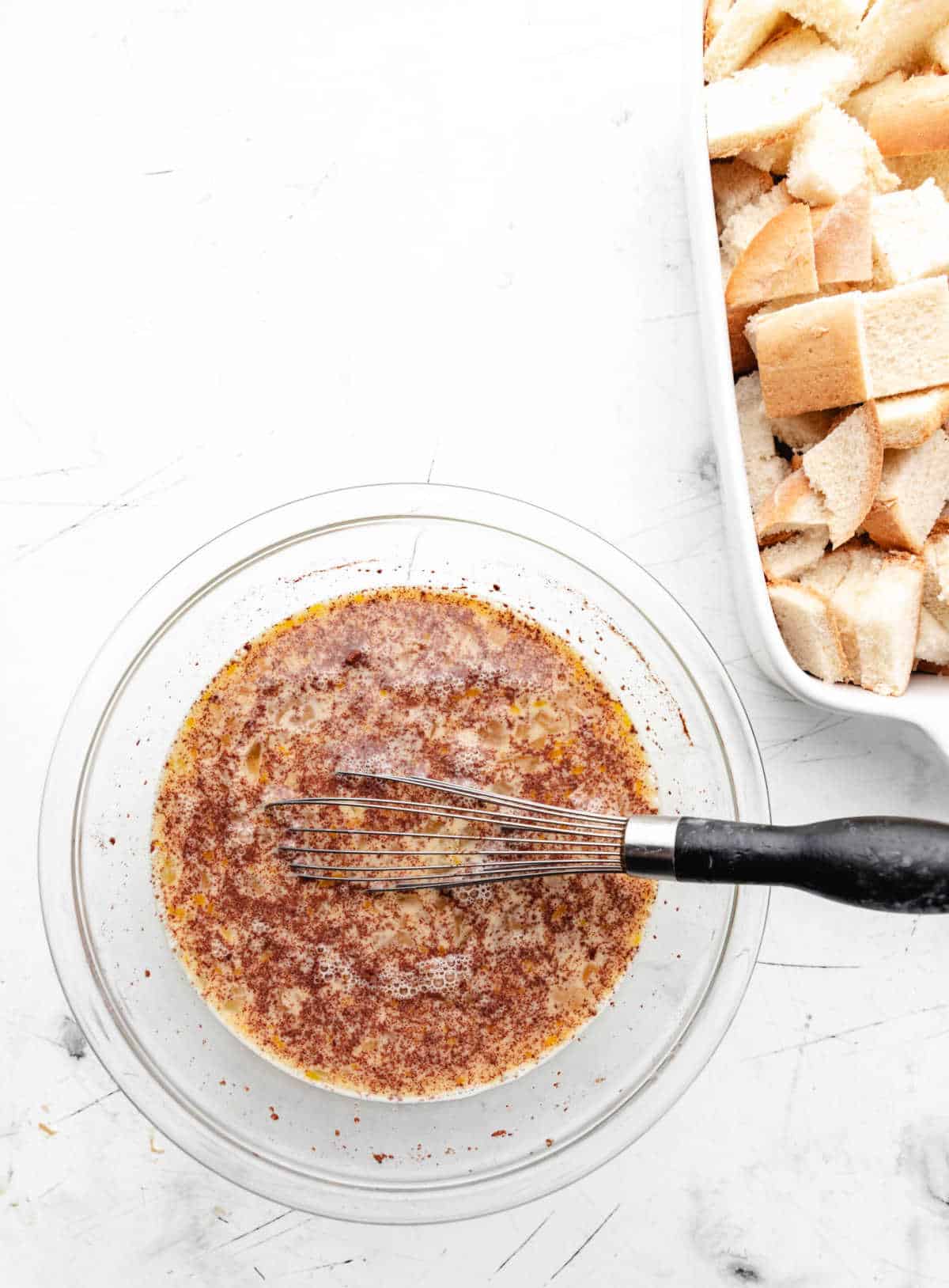 Egg mixture for French toast casserole in a glass mixing bowl with a whisk in it.