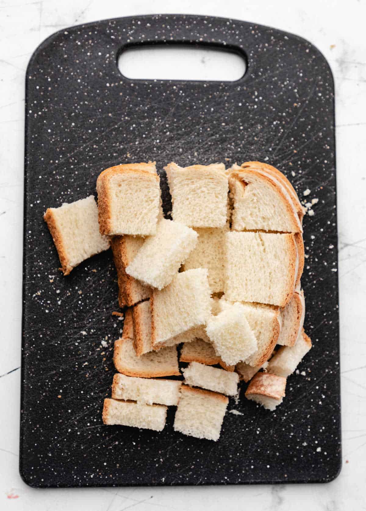 White bread sliced into cubes on a black cutting board. 