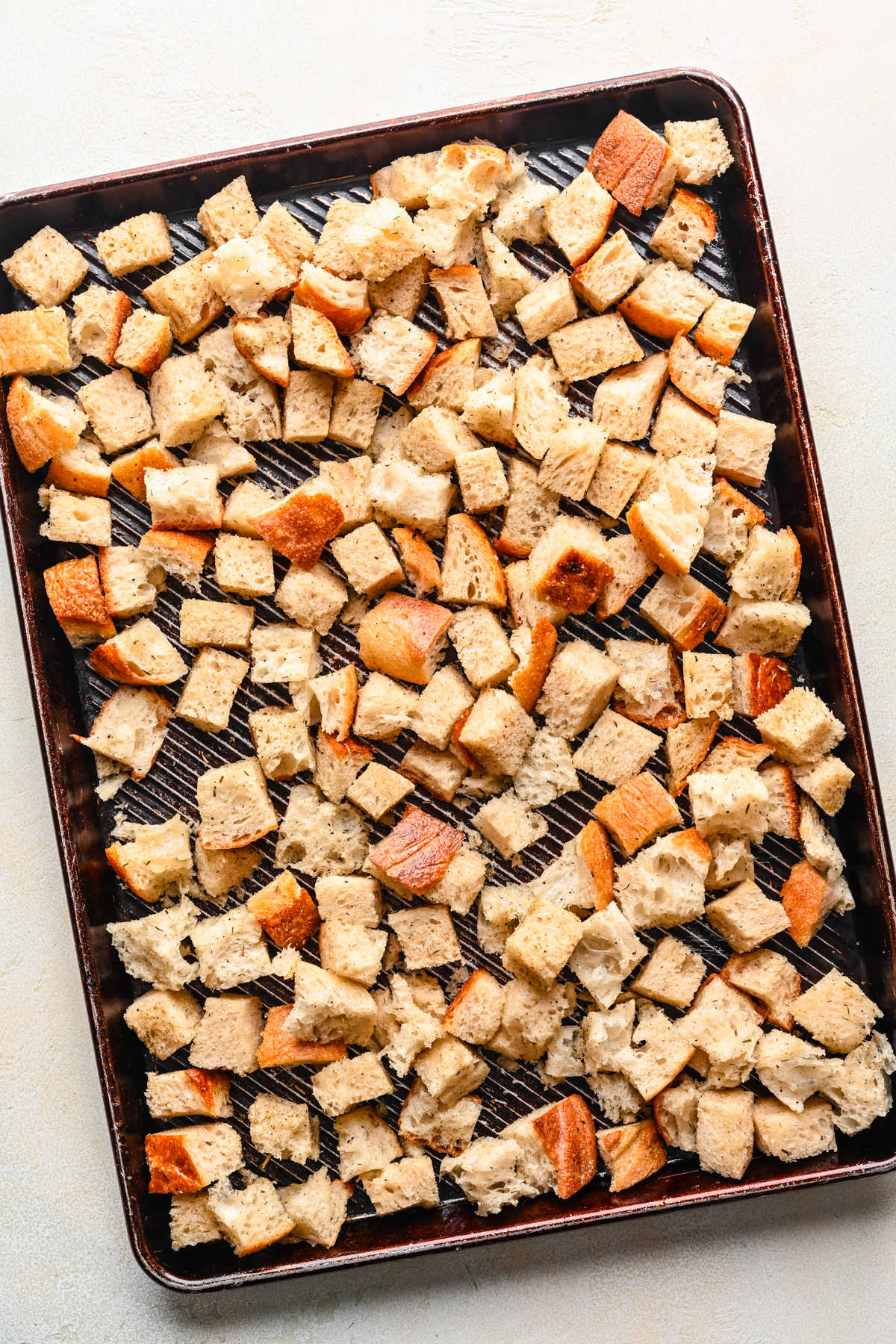 Bread cubes coated in herb olive oil mixture on a baking sheet.