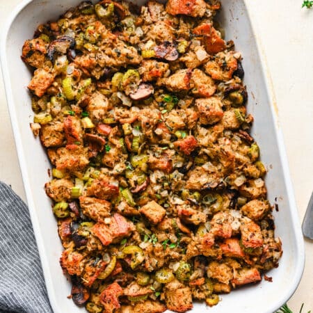 A white dish of baked homemade homemade stuffing next to sprigs of fresh thyme.