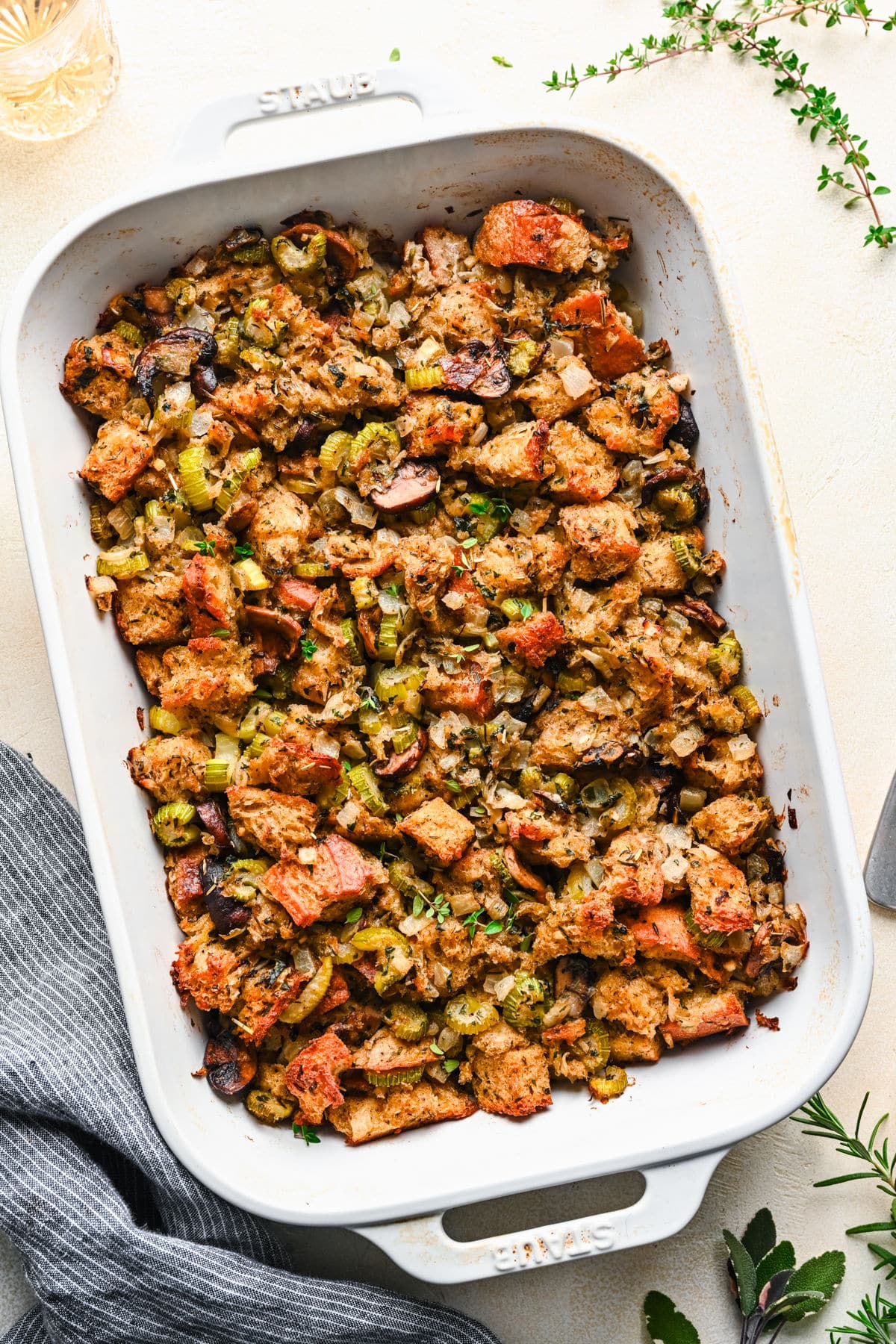 A white dish of baked homemade homemade stuffing next to sprigs of fresh thyme.