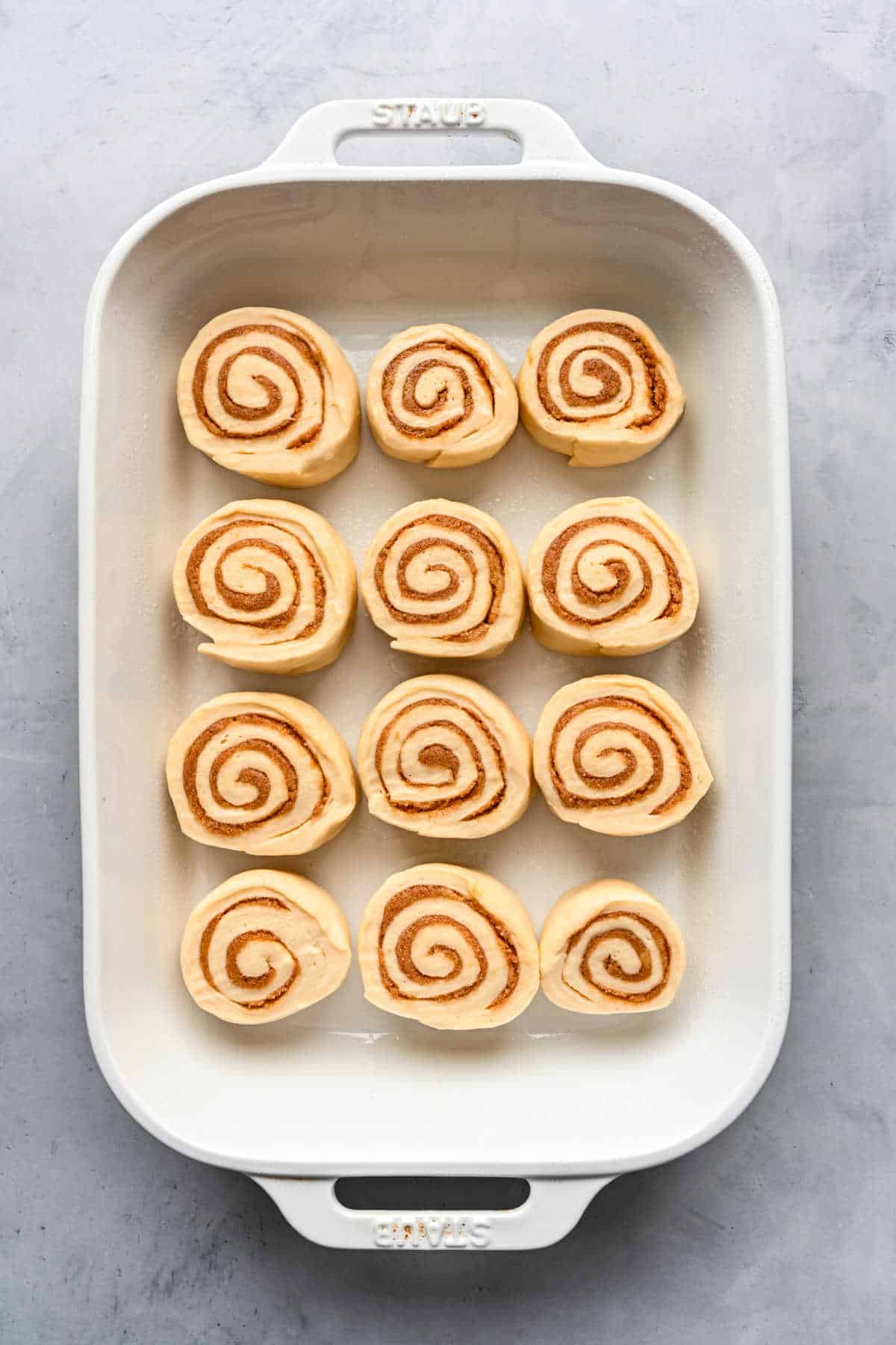 Unbaked maple cinnamon rolls in a white baking pan.