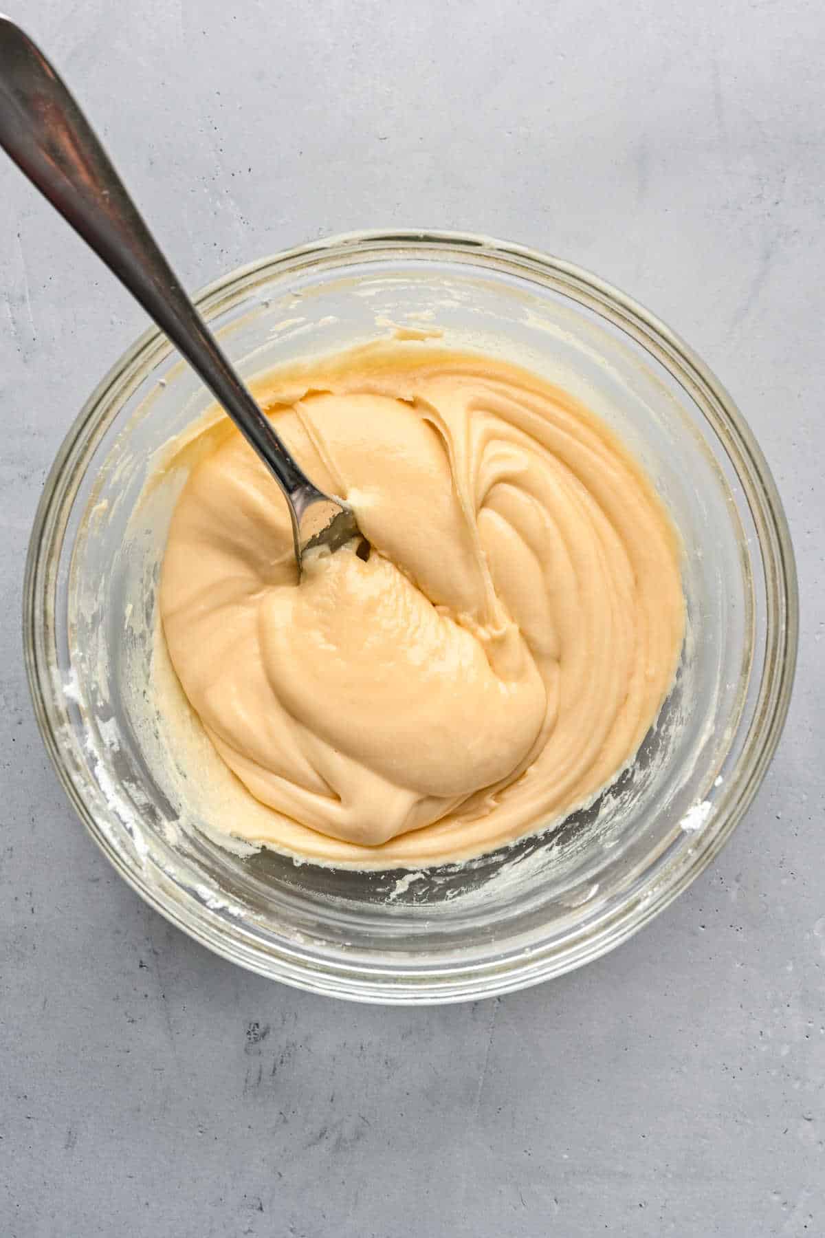 A bowl of maple cinnamon roll frosting in a glass mixing bowl. 