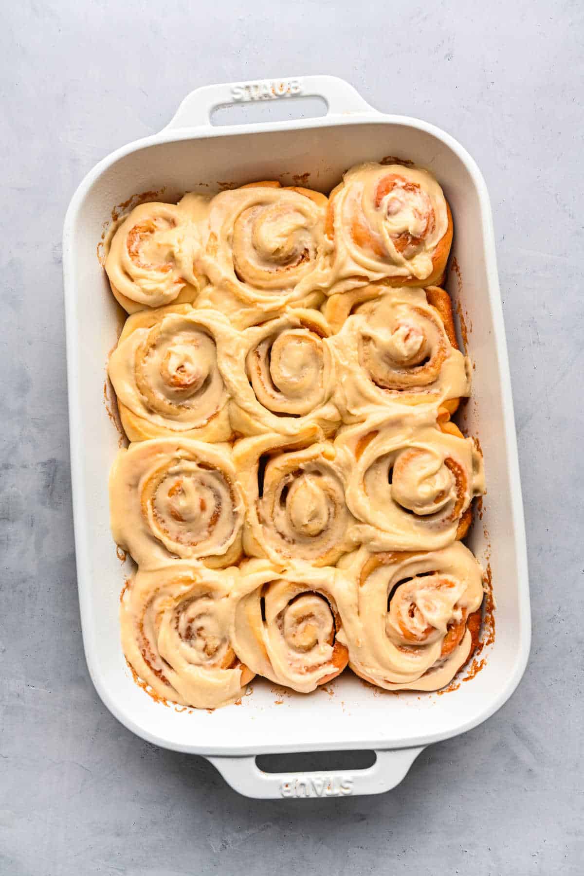 Maple frosted cinnamon rolls in a white baking pan.