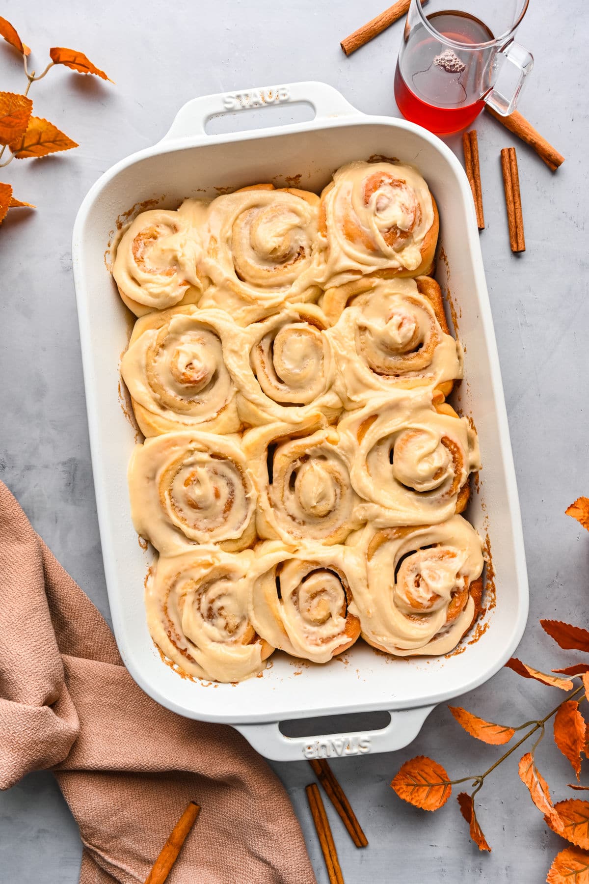 A white baking pan filled with maple iced cinnamon rolls. 