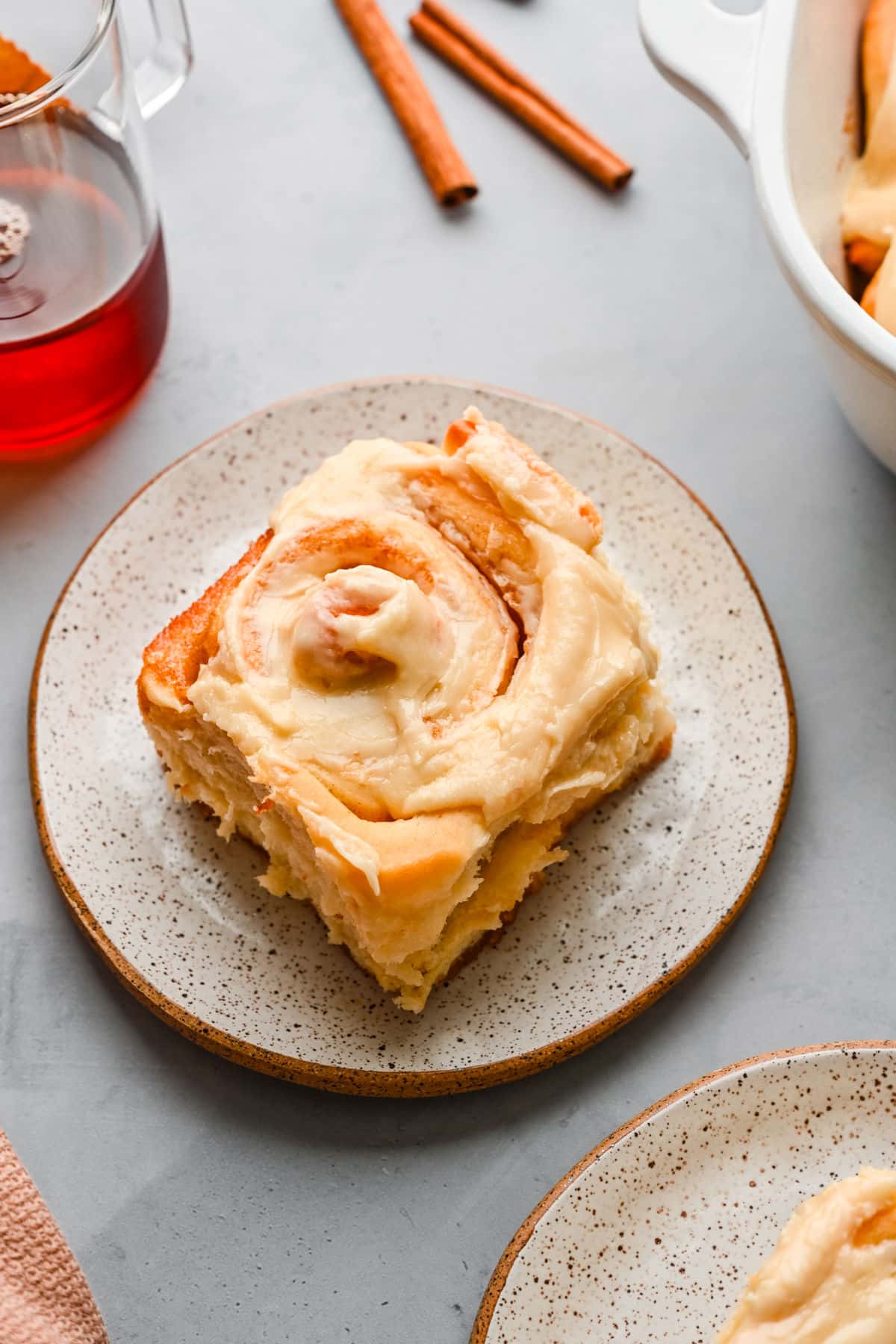 A maple cinnamon roll on a plate next to the dish of cinnamon rolls. 
