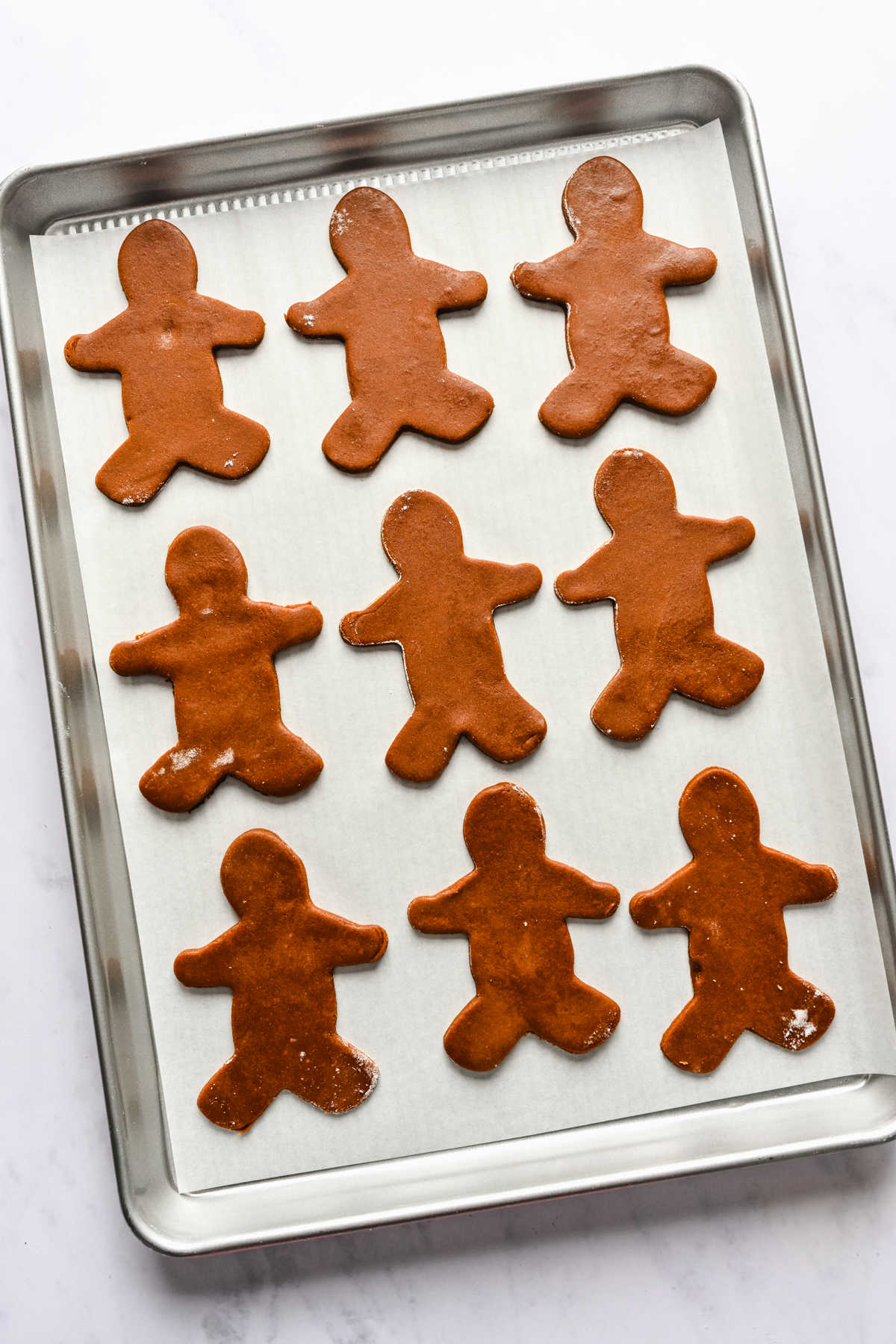 Gingerbread cookie dough cutouts on a baking sheet. 