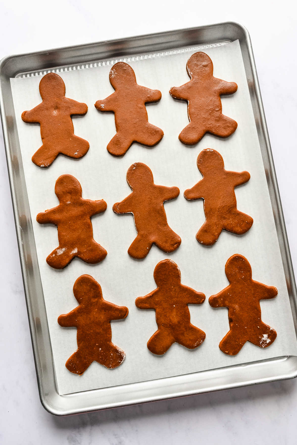 Gingerbread cookie dough cutouts on a baking sheet.
