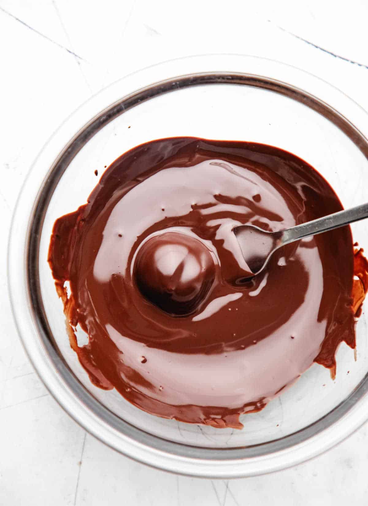 A fork lifting an Oreo cookie ball out of melted chocolate. 