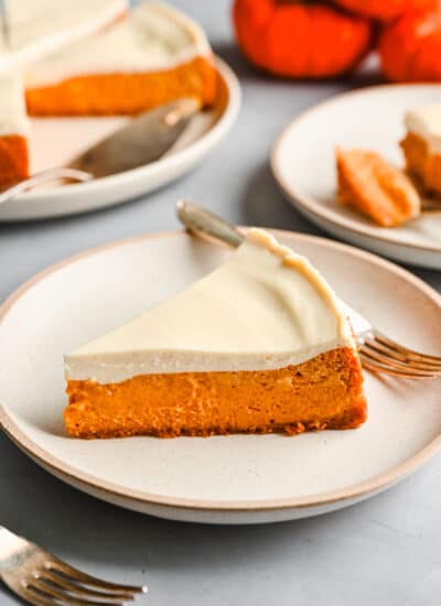 A slice of pumpkin cheesecake on a white plate with a fork next to the cheesecake.