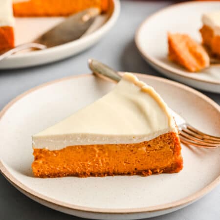 A slice of pumpkin cheesecake on a white plate with a fork next to the cheesecake.