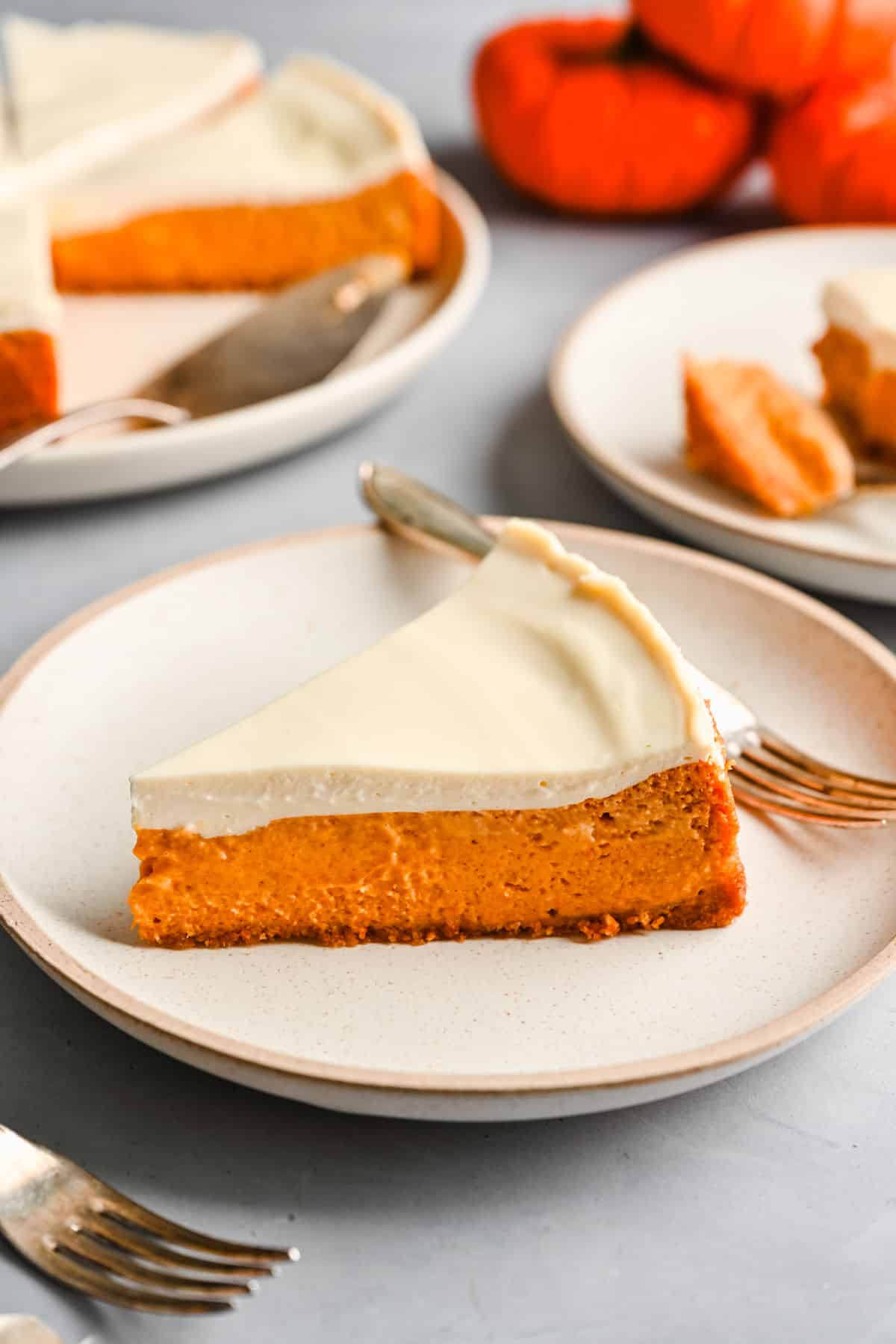 A slice of pumpkin cheesecake on a white plate with a fork next to the cheesecake.