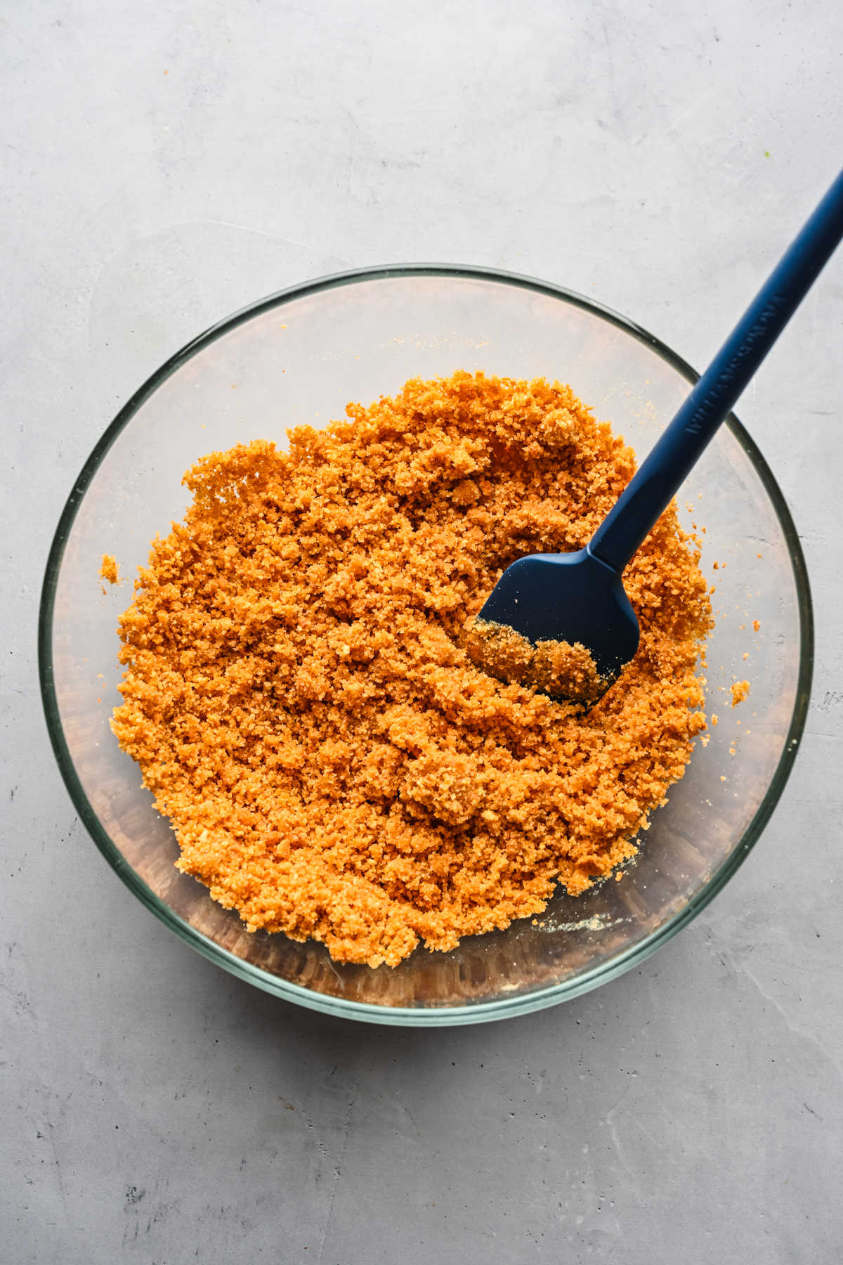 Graham cracker crumbs and melted butter mixed together in a glass mixing bowl. 