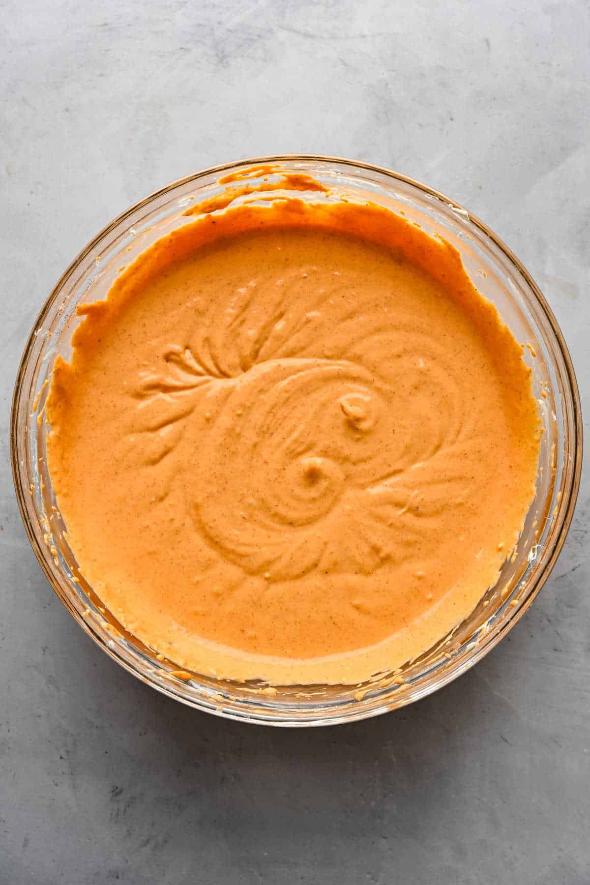 Pumpkin cheesecake mixture in a glass mixing bowl.