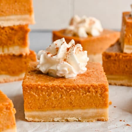 A pumpkin pie bar topped with whipped cream and cinnamon.
